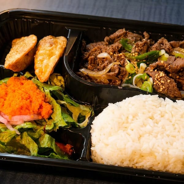 A black bento box with bulgogi, white rice, green salad with orange roe, and two fried dumplings.