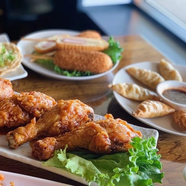 Plates of Korean fried chicken, dumplings with dipping sauce, corn dogs, and a fresh salad.